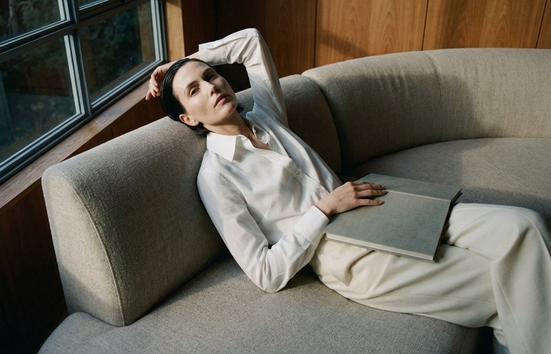A woman Laying on a couch reading a book.