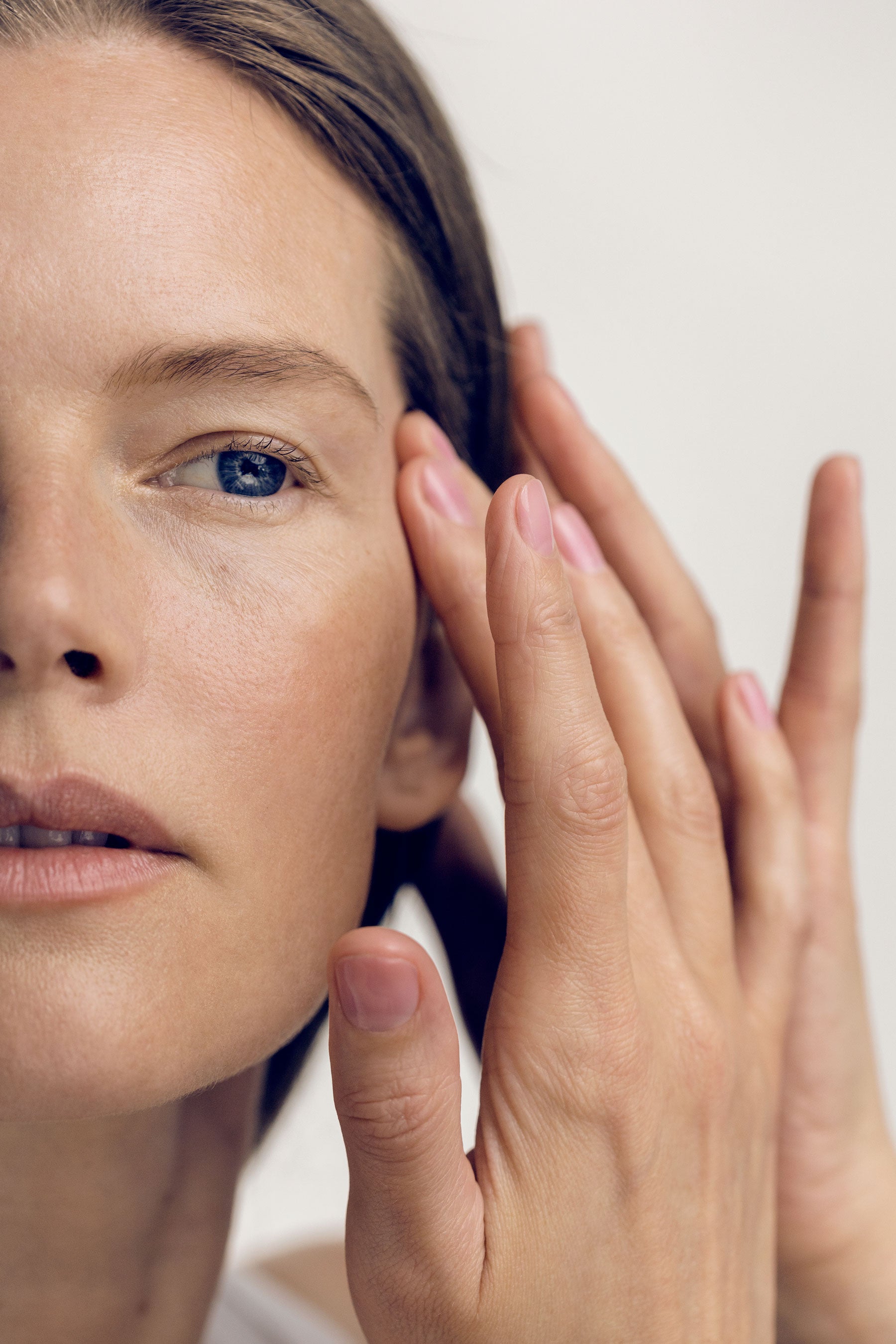 Close-up of a person's face with one hand gently touching their cheek against a white background