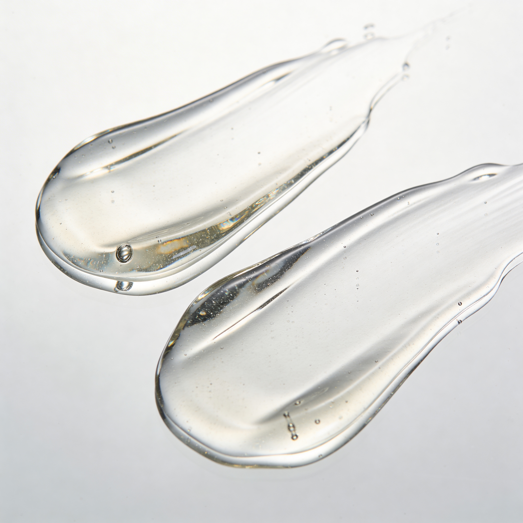 Two clear liquid droplets on a light gray background