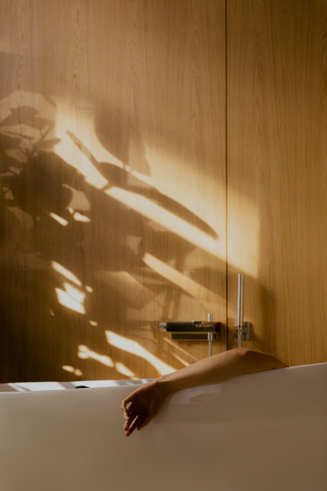 Person in a bathtub with sunlight casting shadows on wooden walls
