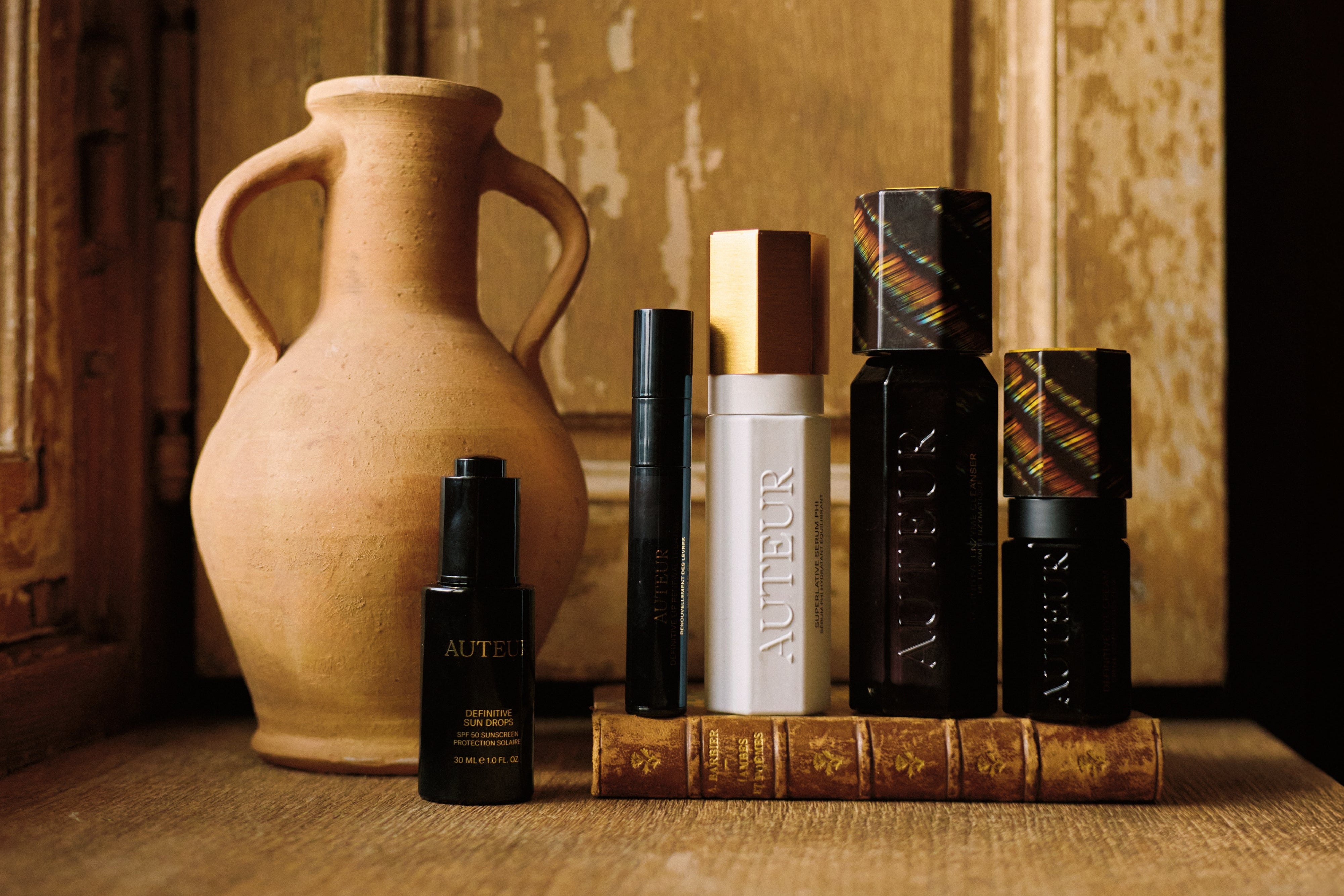 Collection of books and a vase on a wooden surface with a textured wall background