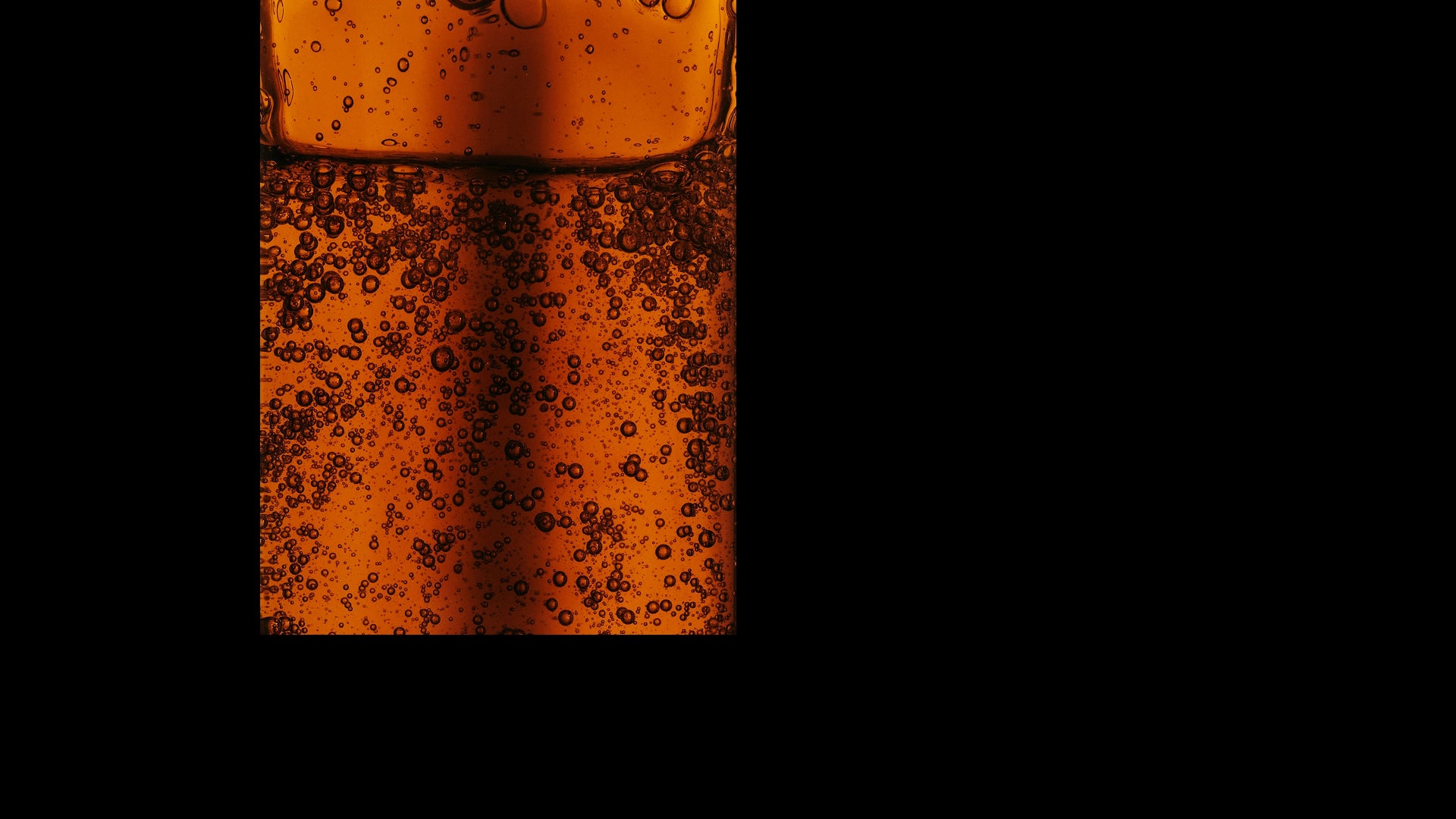 Close-up of a glass with a dark liquid and floating particles on a black background
