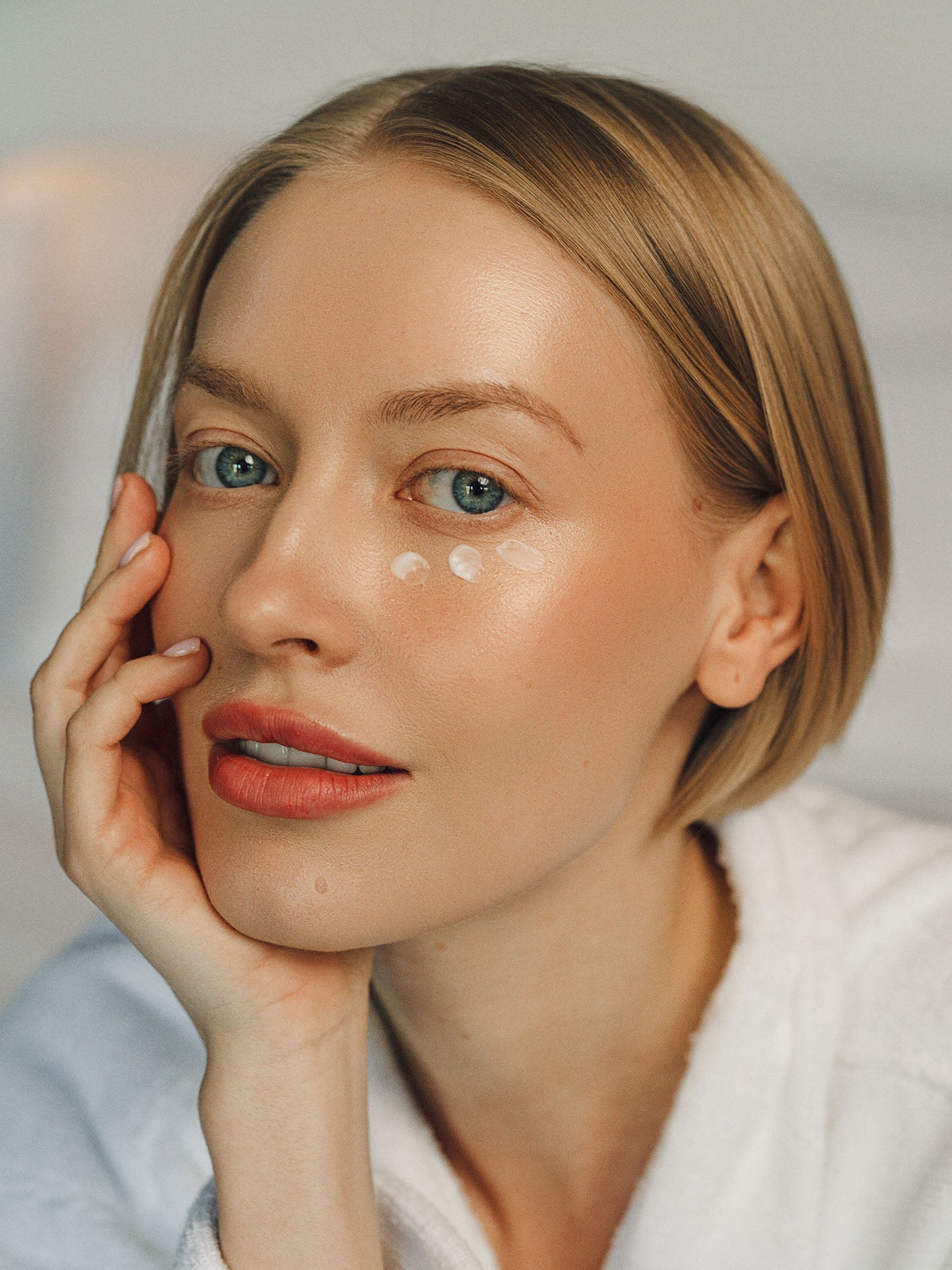 Woman with a soft expression, wearing a white robe, with a neutral background