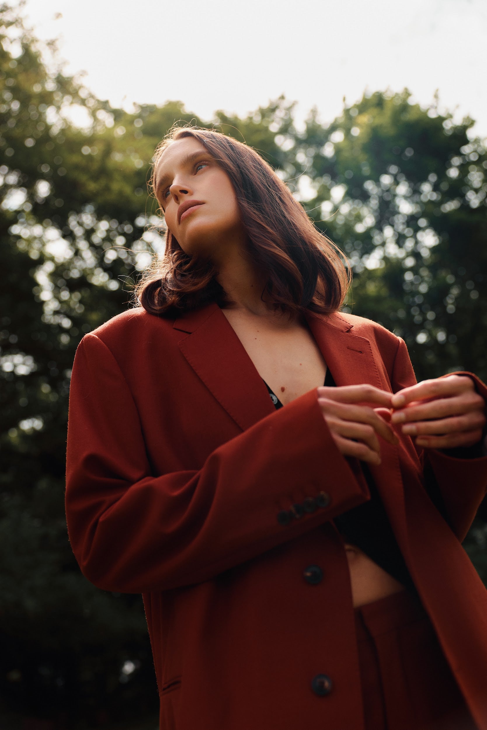 Woman wearing a red coat outdoors with trees in the background