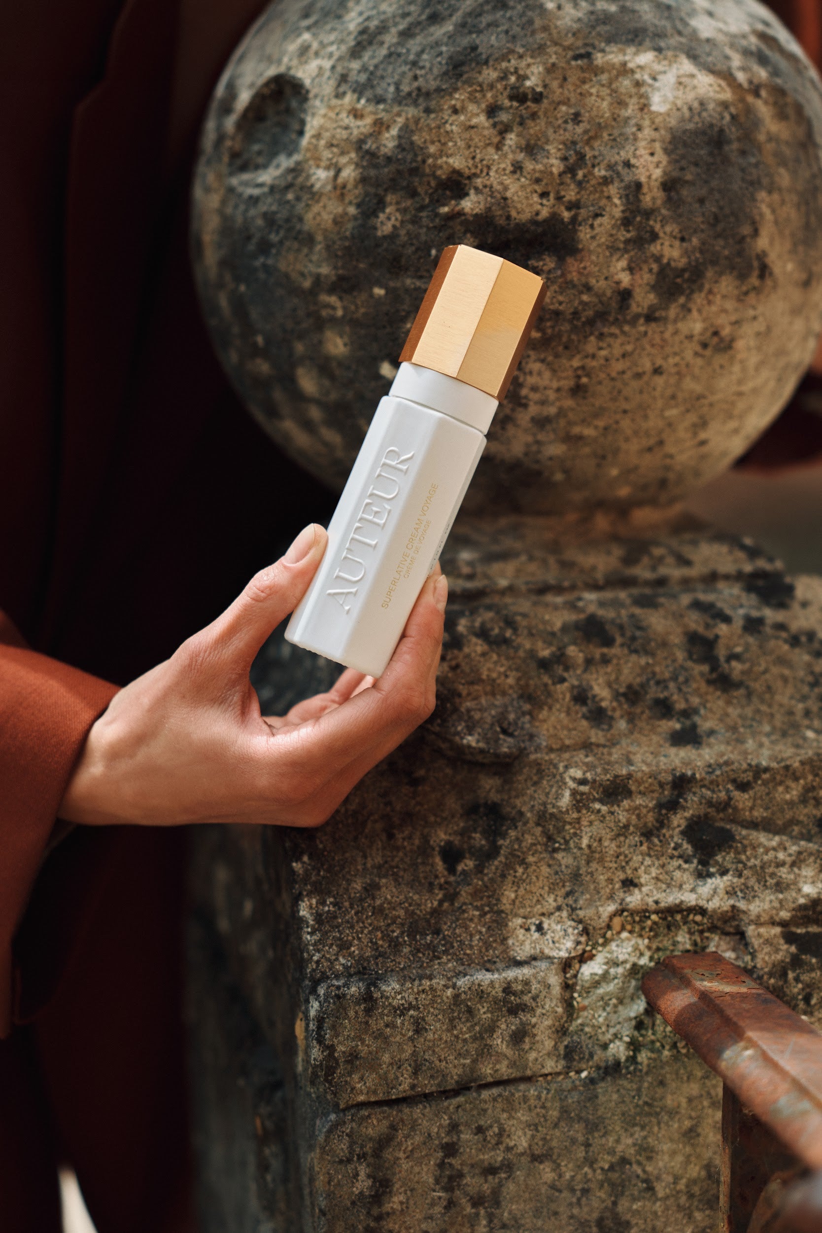 Hand holding a white bottle with gold cap against a textured stone background