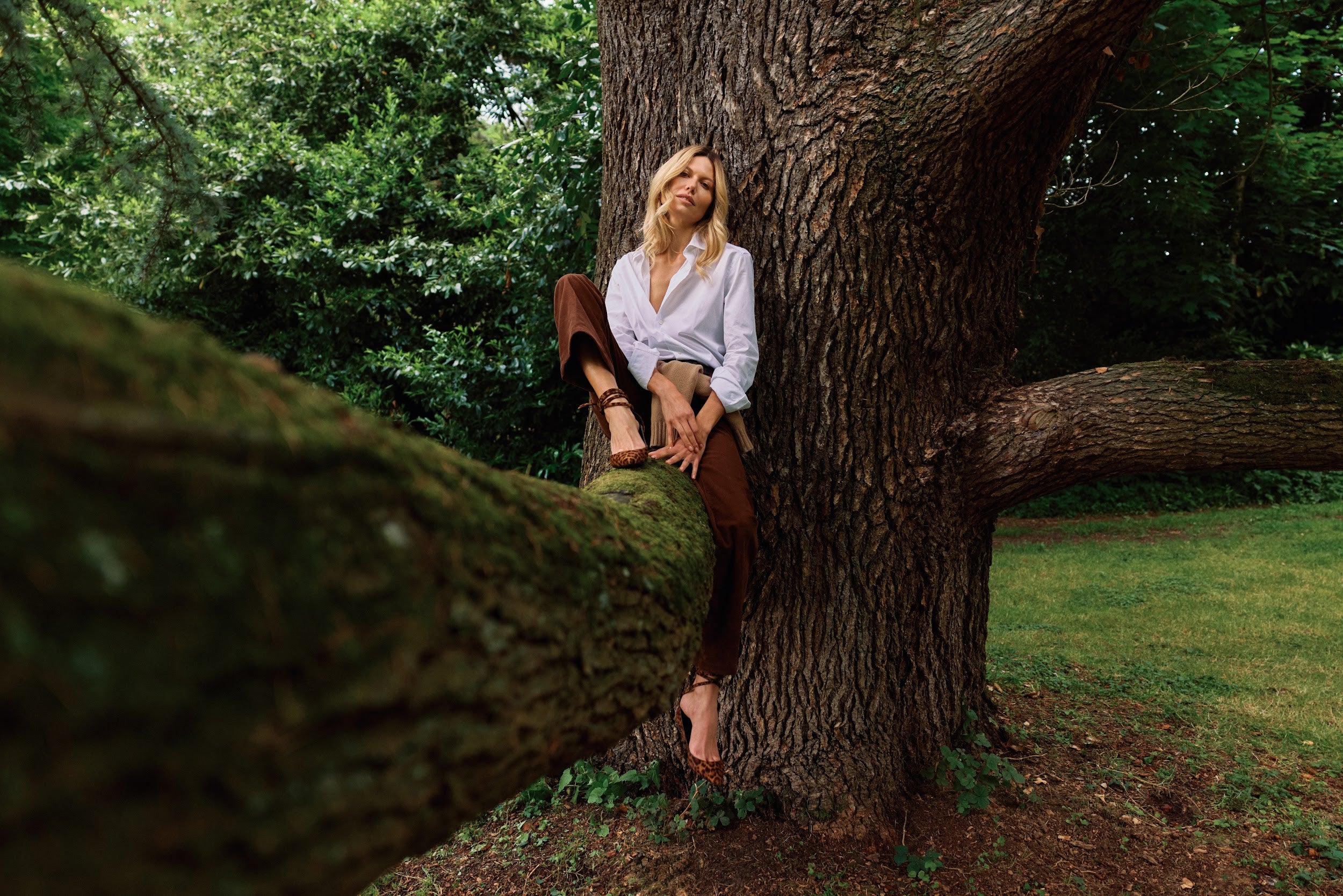 Woman sitting on a large tree branch in a forest setting
