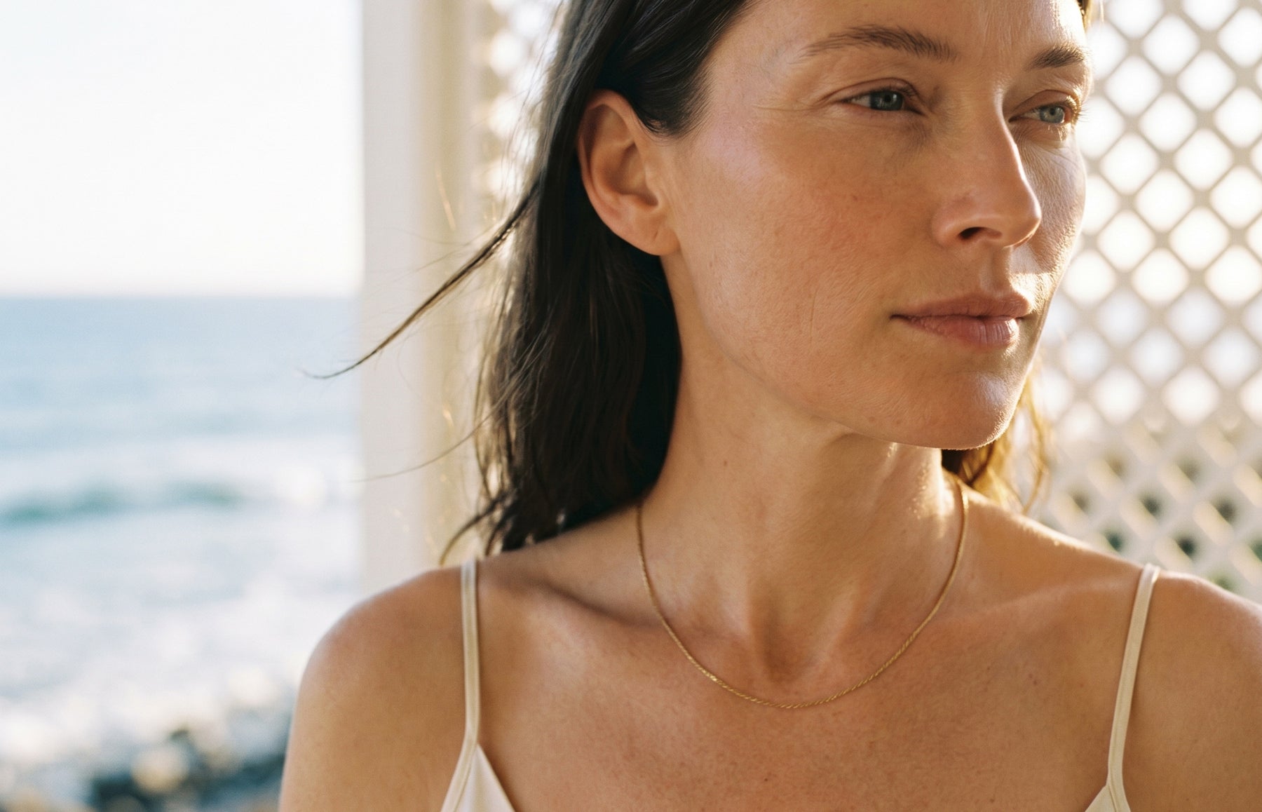 Woman with a necklace standing by a lattice structure with a blurred natural background