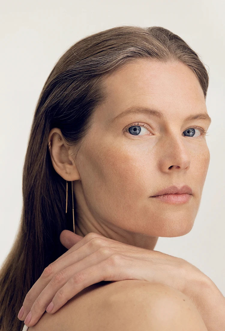 Woman with long brown hair and blue eyes against a plain background